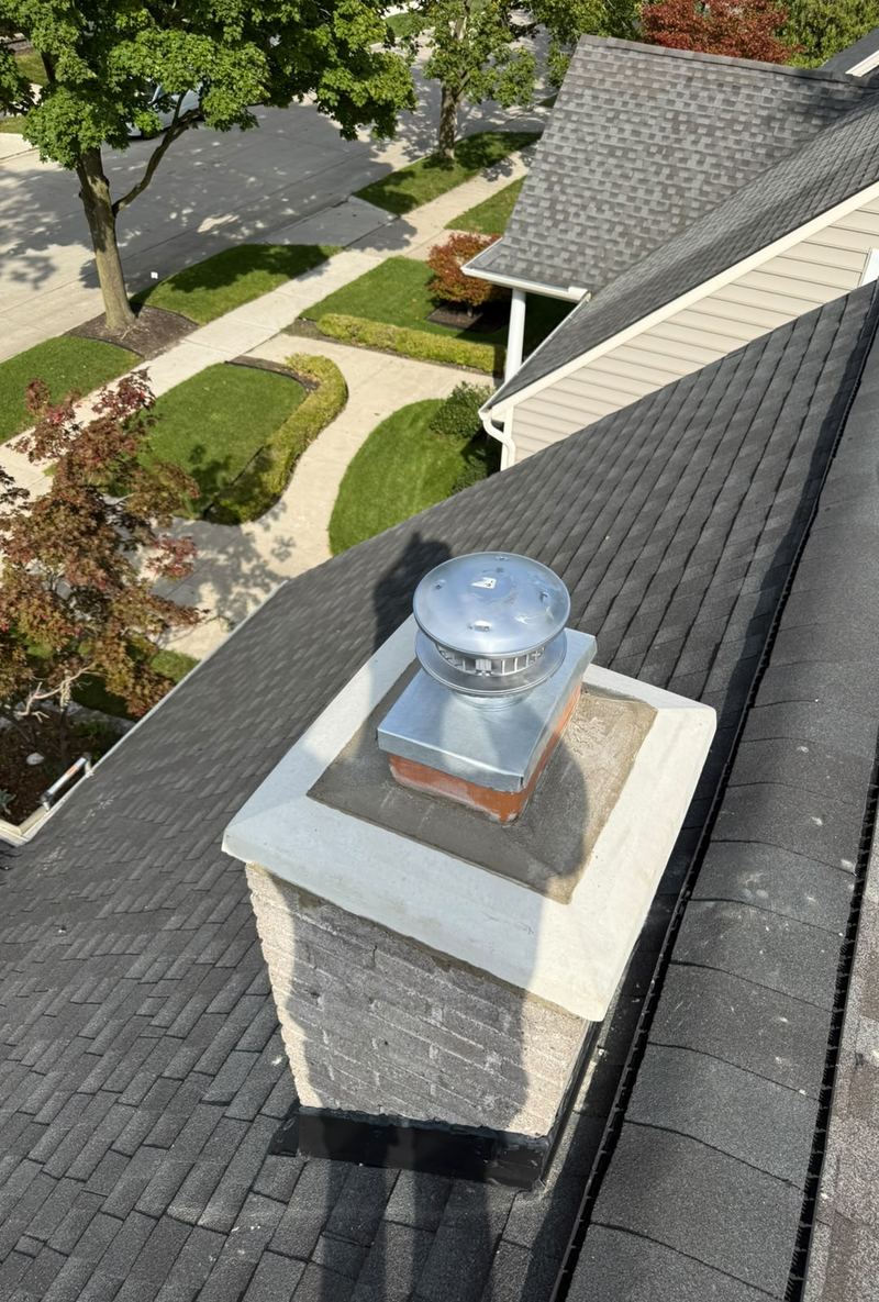Light brick chimney with a white crown and a stainless steel cap, seen from the roof