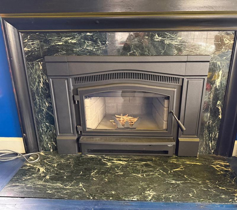 Black wood-burning insert set into a fireplace with a green marble surround